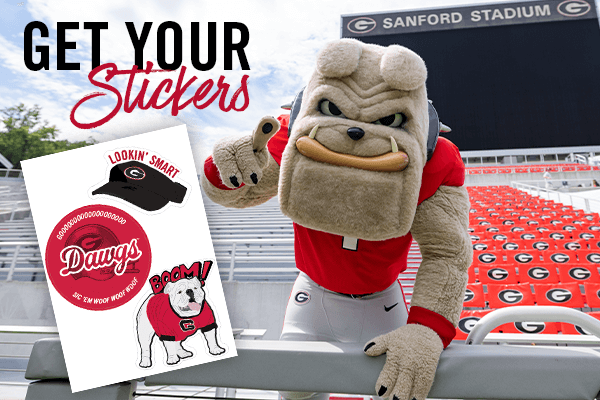 Hairy Dawg in Sanford Stadium in front of jumbotron; foreground text: 'Get Your Stickers', foreground image: sticker sheet with (1) Kirby Smart visor with text 'Lookin' Smart', (2) red circular sticker with football helmet, text: 'Gooooooooooooooooooo DAWGS sic 'em woof woof woof, (3) drawn image of Boom the bulldog mascot with text 'BOOM!'